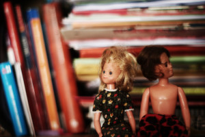 Zwei Puppen sitzen im Bücherregal.
